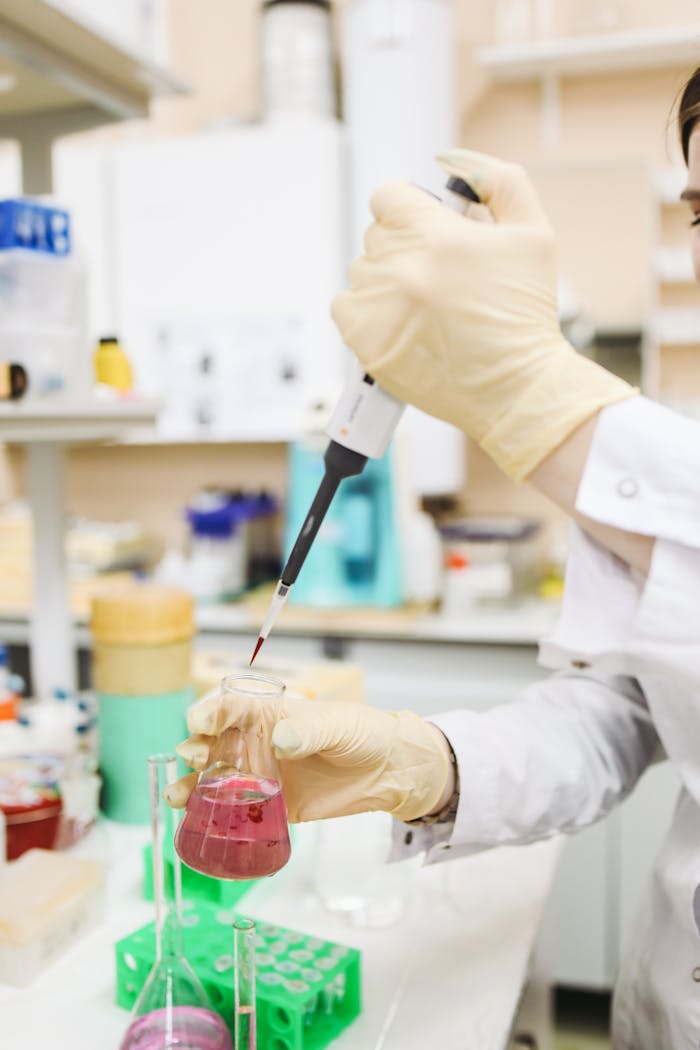 A laboratory technician uses a pipette to transfer red liquid into a beaker in a science lab.